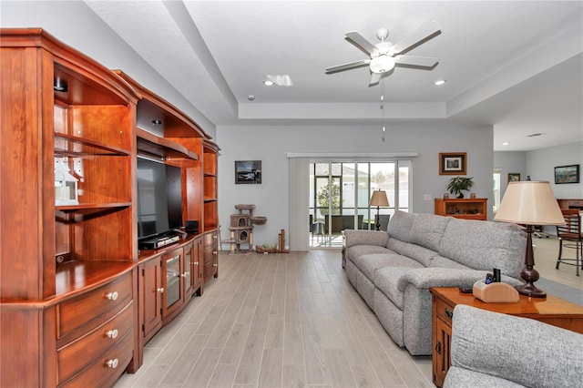 living area with recessed lighting, a raised ceiling, light wood-style floors, and a ceiling fan