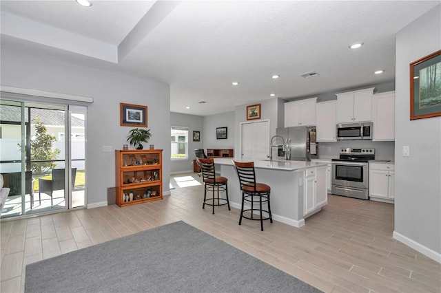 kitchen with visible vents, wood finish floors, a breakfast bar, white cabinets, and stainless steel appliances