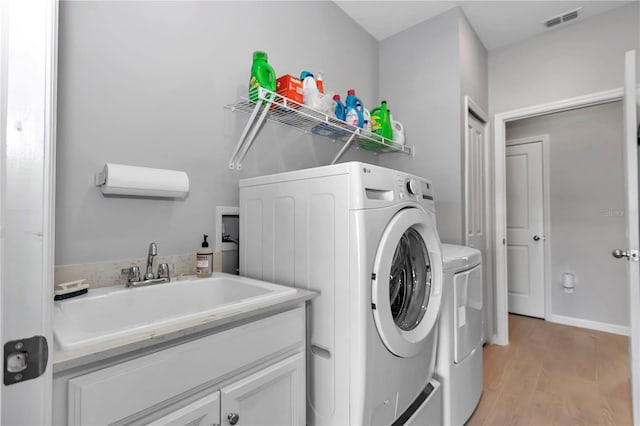 clothes washing area featuring washing machine and dryer, visible vents, light wood finished floors, and a sink