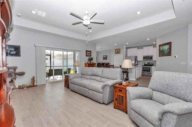 living room featuring recessed lighting, light wood-style flooring, a raised ceiling, and ceiling fan