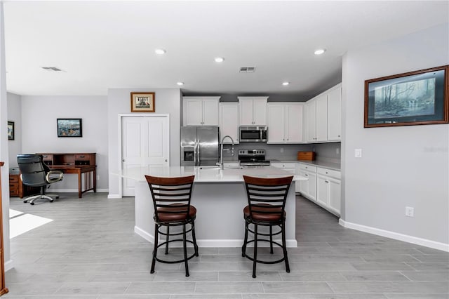 kitchen with visible vents, a breakfast bar area, light countertops, stainless steel appliances, and white cabinetry