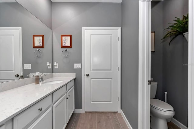 bathroom featuring toilet, vanity, baseboards, and wood finished floors