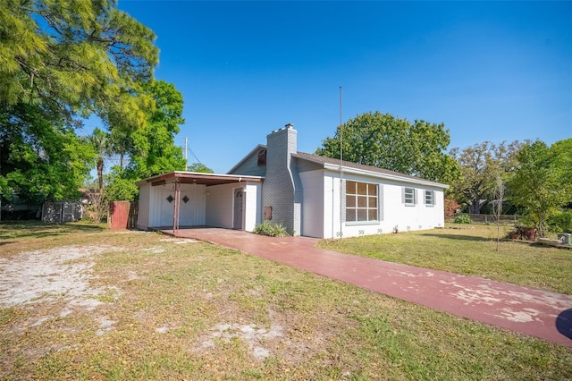 single story home with a front yard, a carport, and a chimney