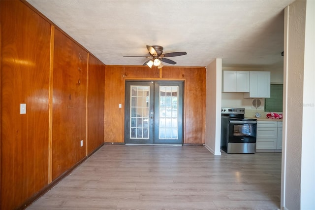 interior space with french doors, ceiling fan, wood walls, and light wood finished floors