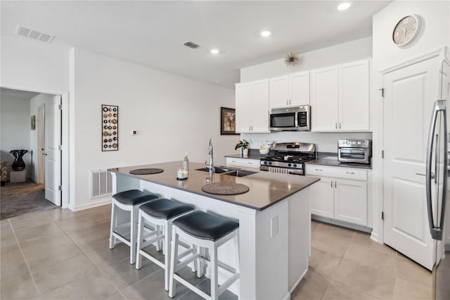 kitchen with a sink, stainless steel appliances, dark countertops, and visible vents