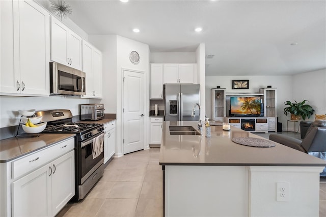 kitchen with an island with sink, a sink, open floor plan, appliances with stainless steel finishes, and white cabinets