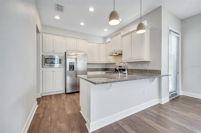 kitchen with visible vents, a sink, dark stone countertops, stainless steel appliances, and a peninsula