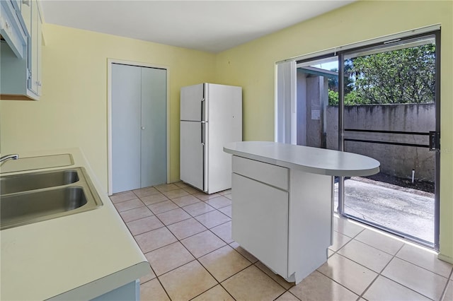 kitchen with a sink, light tile patterned floors, light countertops, and freestanding refrigerator