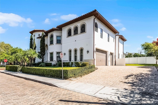 mediterranean / spanish home featuring fence, a tiled roof, stucco siding, decorative driveway, and a garage