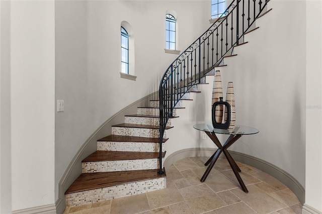 stairway featuring stone finish flooring, a high ceiling, and baseboards