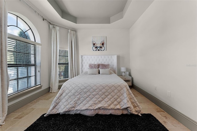 bedroom featuring multiple windows, a raised ceiling, baseboards, and stone tile flooring