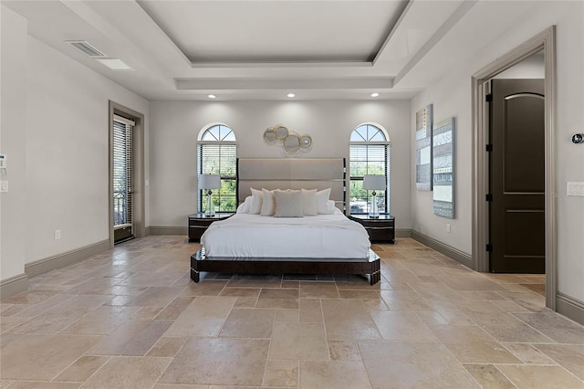 bedroom with a tray ceiling, multiple windows, baseboards, and stone tile flooring