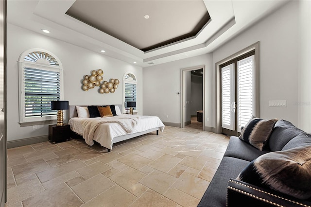 bedroom with stone tile floors, baseboards, a tray ceiling, and access to exterior