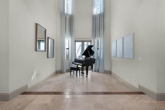 hallway featuring baseboards, stone tile flooring, and a towering ceiling