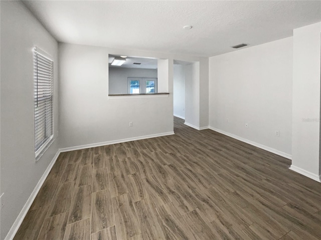 unfurnished room featuring dark wood-type flooring, baseboards, visible vents, and a textured ceiling