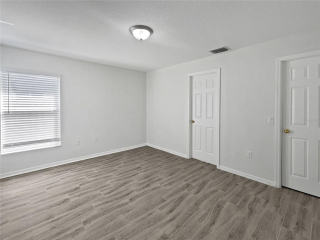 spare room featuring a textured ceiling, wood finished floors, visible vents, and baseboards