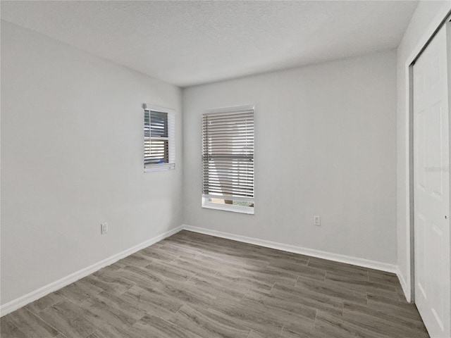 unfurnished bedroom featuring wood finished floors, baseboards, a closet, and a textured ceiling