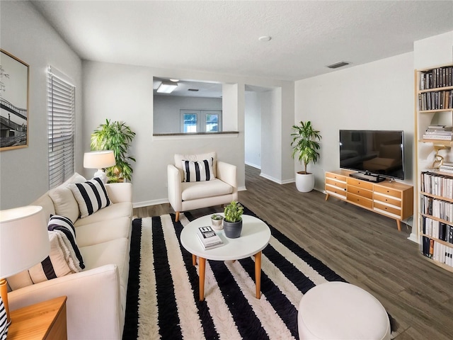 living room featuring visible vents, a textured ceiling, baseboards, and wood finished floors