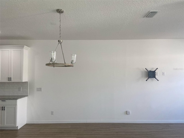 unfurnished dining area with baseboards, visible vents, dark wood-style flooring, a textured ceiling, and a chandelier