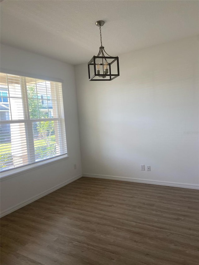 spare room with an inviting chandelier, baseboards, and dark wood-type flooring