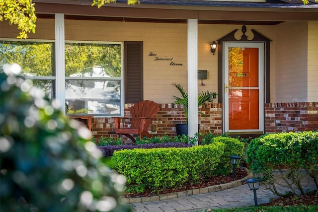 doorway to property featuring brick siding and a porch