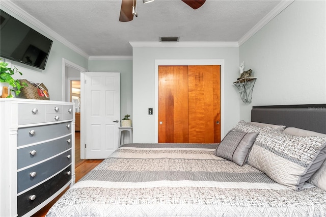 bedroom featuring visible vents, a textured ceiling, wood finished floors, and crown molding