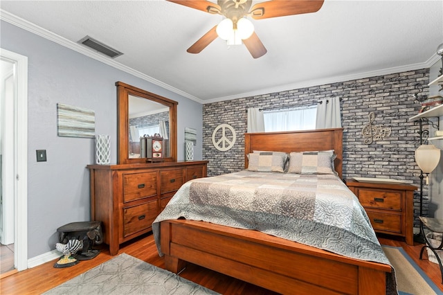 bedroom featuring visible vents, brick wall, crown molding, and wood finished floors