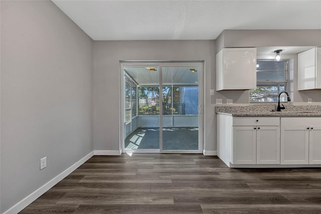 kitchen with white cabinetry, dark wood-type flooring, baseboards, and a sink