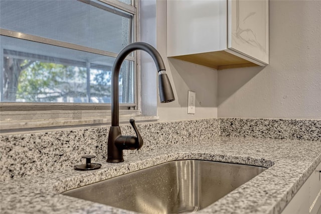 interior details featuring a sink, a textured wall, light stone counters, and white cabinetry