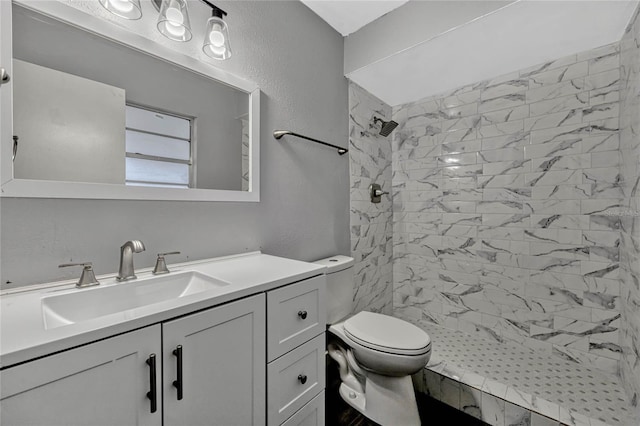 bathroom with tiled shower, toilet, vanity, and a textured wall