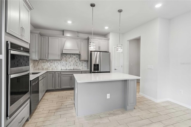 kitchen featuring gray cabinetry, custom range hood, a center island, stainless steel appliances, and decorative backsplash