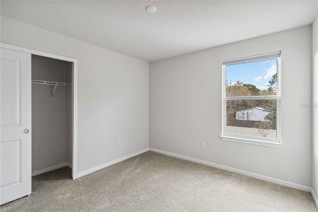 unfurnished bedroom featuring baseboards, light carpet, a textured ceiling, and a closet