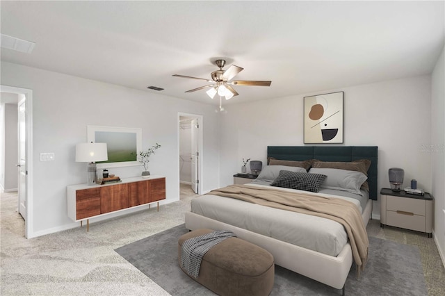 carpeted bedroom featuring visible vents, baseboards, a walk in closet, and a ceiling fan