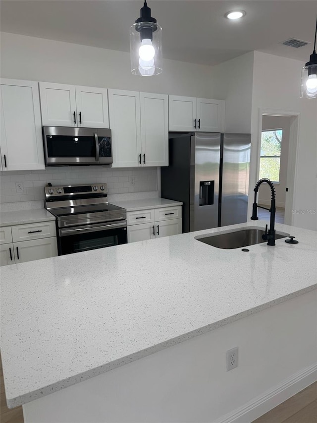 kitchen with light stone counters, a sink, decorative backsplash, stainless steel appliances, and white cabinetry