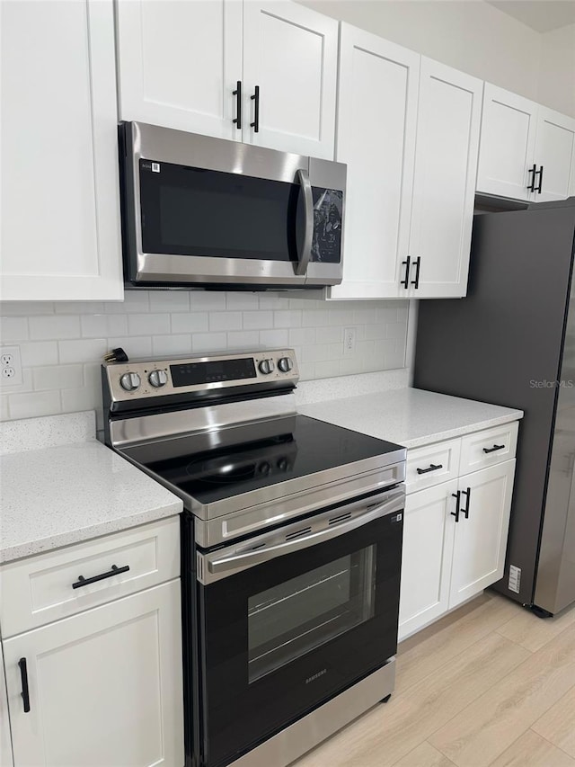 kitchen with tasteful backsplash, white cabinets, appliances with stainless steel finishes, and light wood-style floors