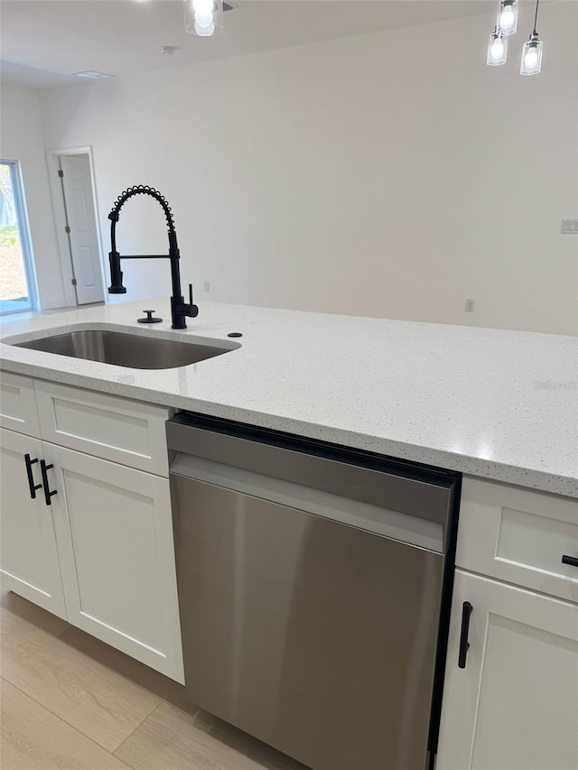 kitchen with pendant lighting, light stone counters, stainless steel dishwasher, white cabinets, and a sink