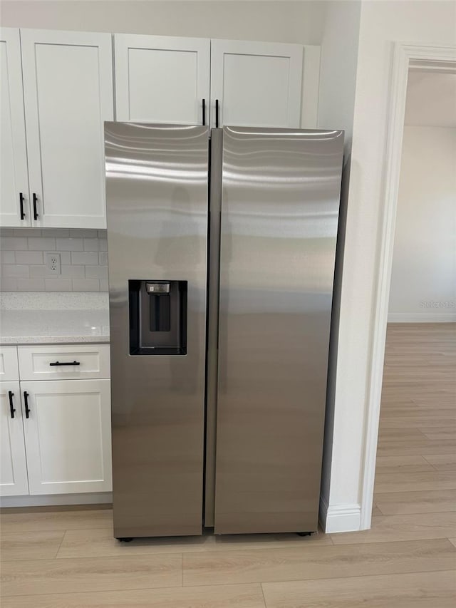 kitchen with light countertops, light wood-style floors, white cabinetry, stainless steel fridge, and backsplash