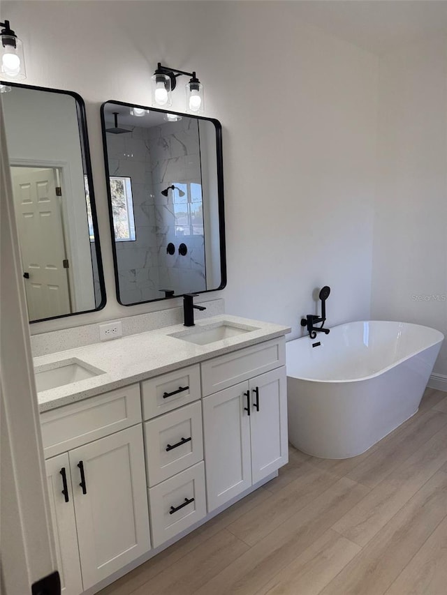 bathroom featuring a freestanding tub, a sink, wood finished floors, a marble finish shower, and double vanity