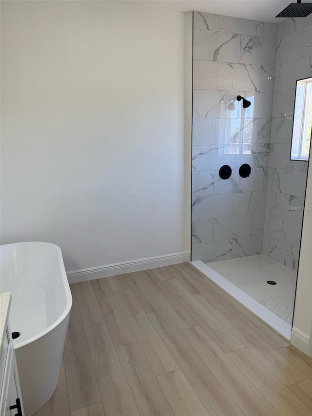 bathroom with a freestanding tub, baseboards, wood finished floors, and a tile shower