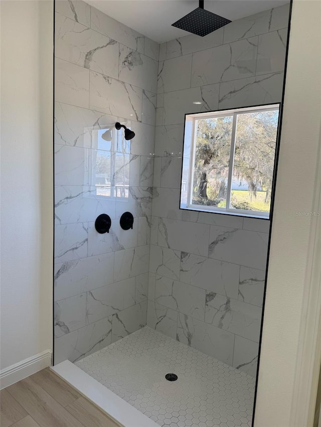 bathroom with wood finished floors, baseboards, and a tile shower