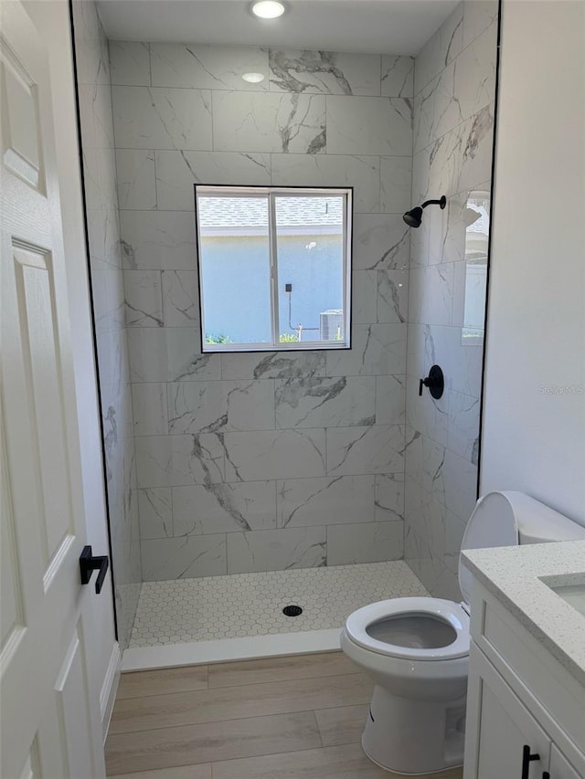 bathroom with a tile shower, toilet, vanity, and wood finished floors