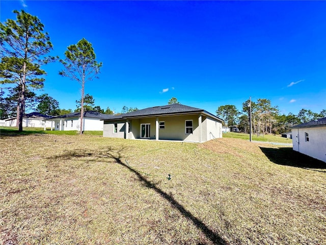 rear view of property featuring a lawn and stucco siding