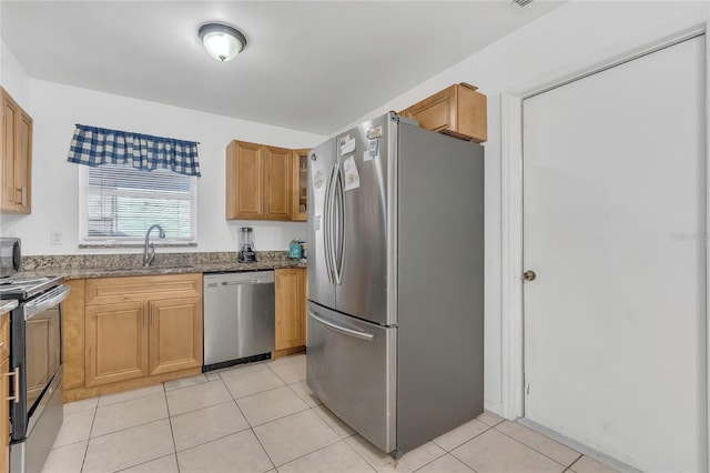 kitchen featuring dark stone counters, light tile patterned floors, appliances with stainless steel finishes, and a sink