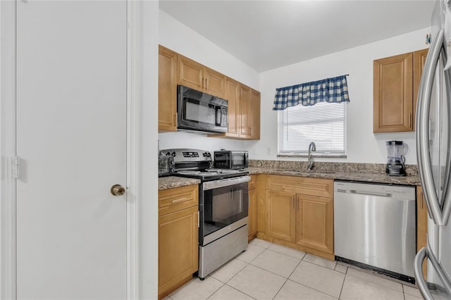 kitchen with stone countertops, a sink, stainless steel appliances, a toaster, and light tile patterned floors