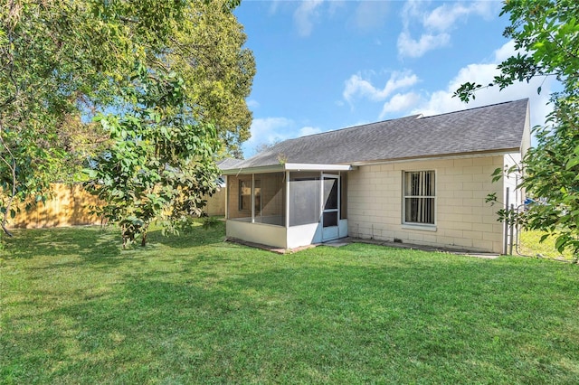 back of property with a lawn, a sunroom, roof with shingles, and fence