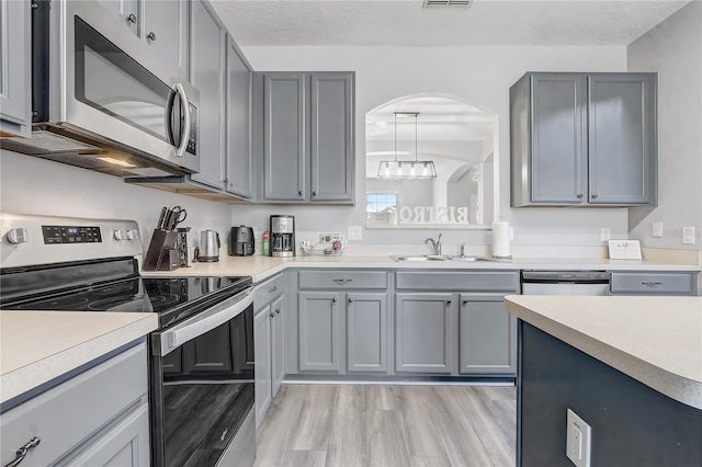 1028 Orange Cosmos Blvd, Davenport, FL 33837 - kitchen featuring stainless steel appliances, gray cabinetry, light countertops, light wood-style flooring, and arched walkways