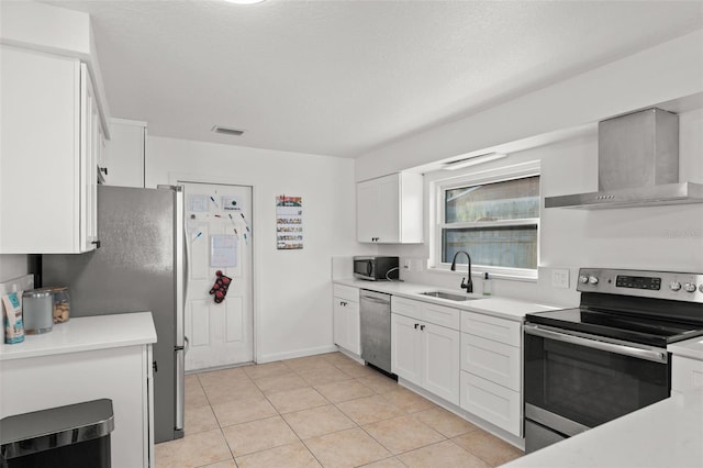 kitchen featuring visible vents, wall chimney range hood, stainless steel appliances, white cabinetry, and a sink