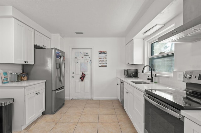 kitchen with a sink, light countertops, appliances with stainless steel finishes, white cabinetry, and wall chimney range hood