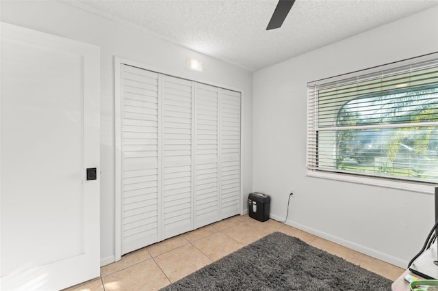 unfurnished bedroom with a ceiling fan, a textured ceiling, a closet, light tile patterned floors, and baseboards