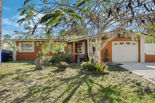 ranch-style home with an outdoor fire pit, concrete driveway, a front yard, stucco siding, and an attached garage